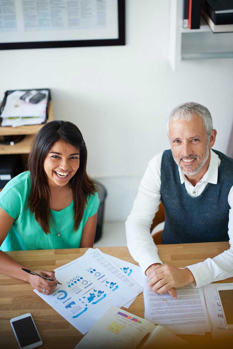 a woman and a man sitting at a table with financial paperwork smiling at the camera