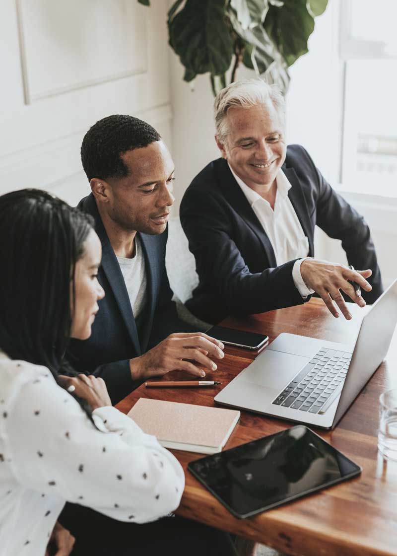 two men and a woman looking at a laptop in a business office